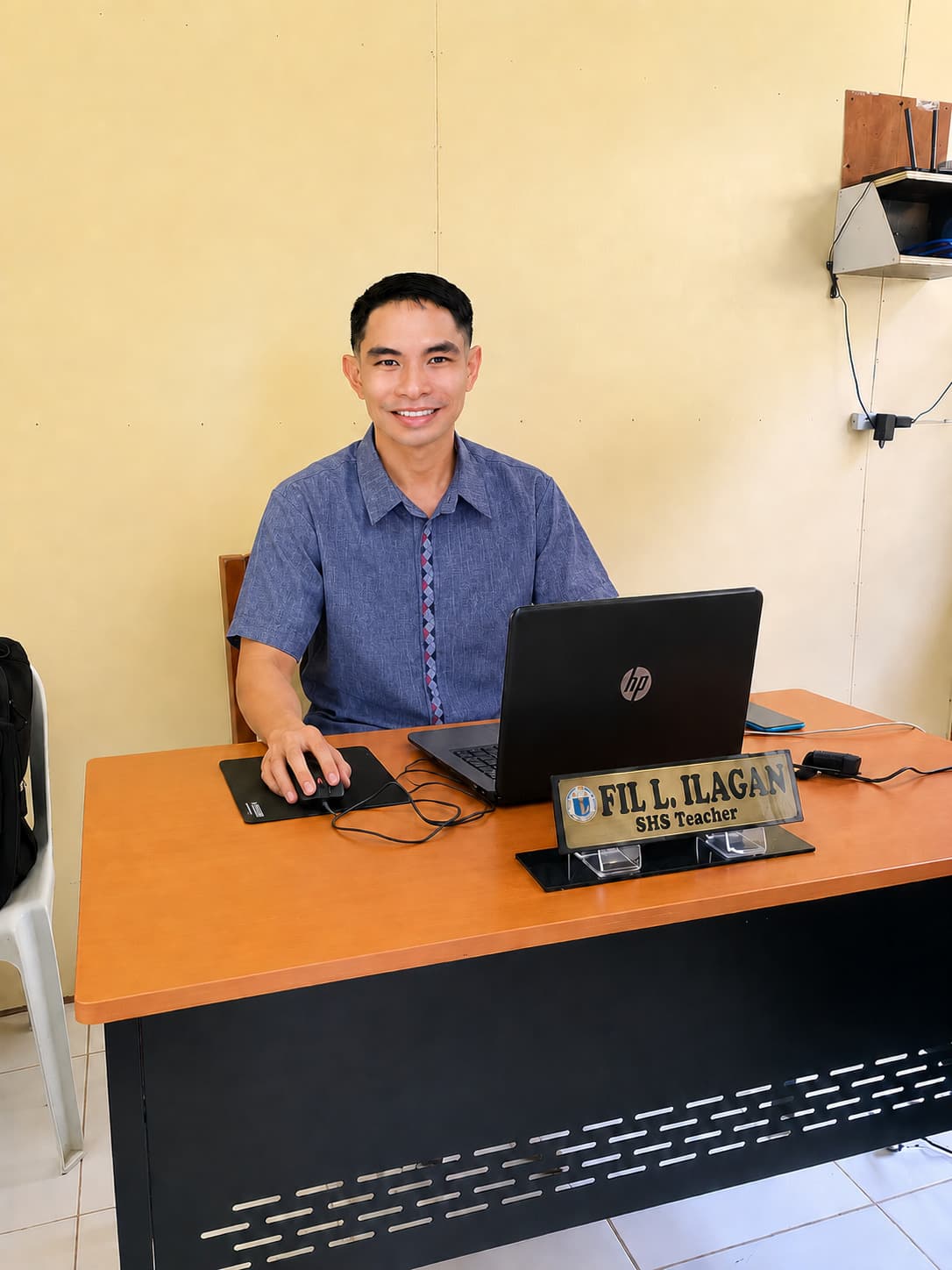 Fil Ilagan working on a laptop at his desk; his nameplate reads 'Fil L. Ilagan · SHS Teacher.'
